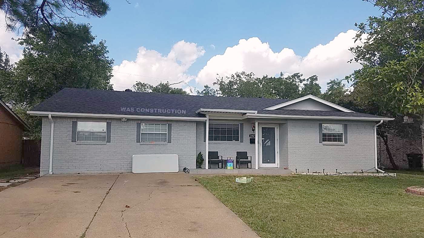 A grey brick ranch home with a finished roof and a clear driveway