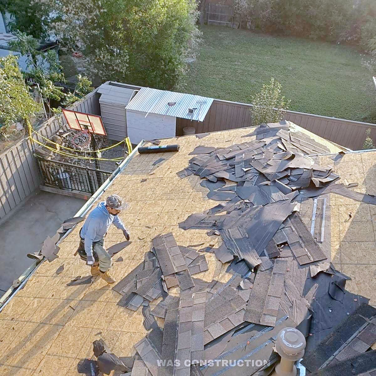A pile of torn-off shingles on bare decking during a tear-off