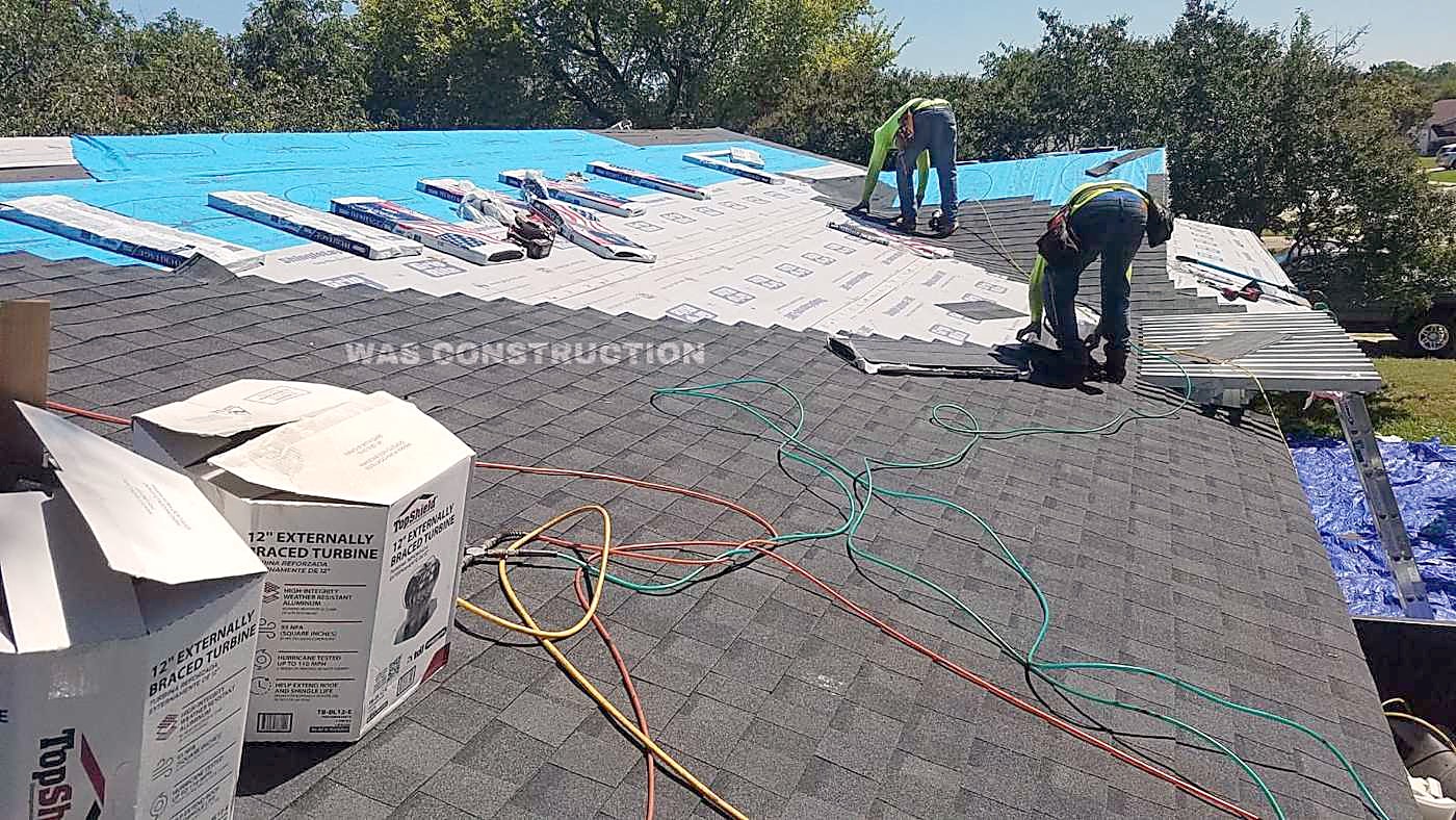 Blue underlayment down over a stripped roof with the crew still working