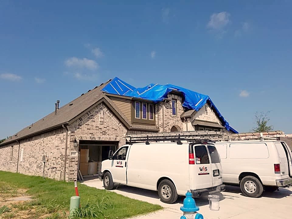 A WAS Construction van in a driveway with a blue tarp over the damaged roof